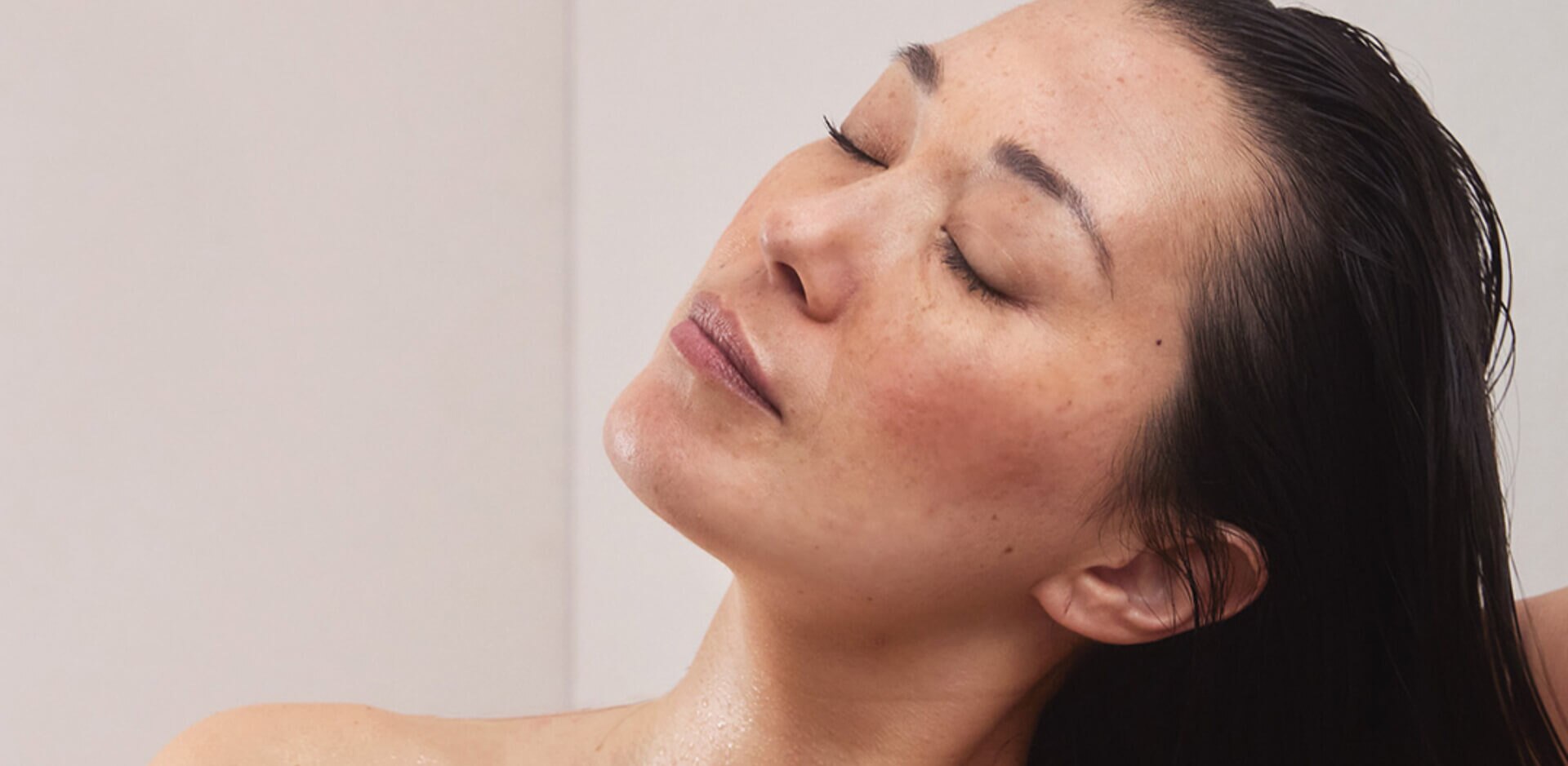 Close-up van een vrouw die met gesloten ogen en haar hoofd achterover geniet van een moment van ontspanning, mogelijk in de douche.