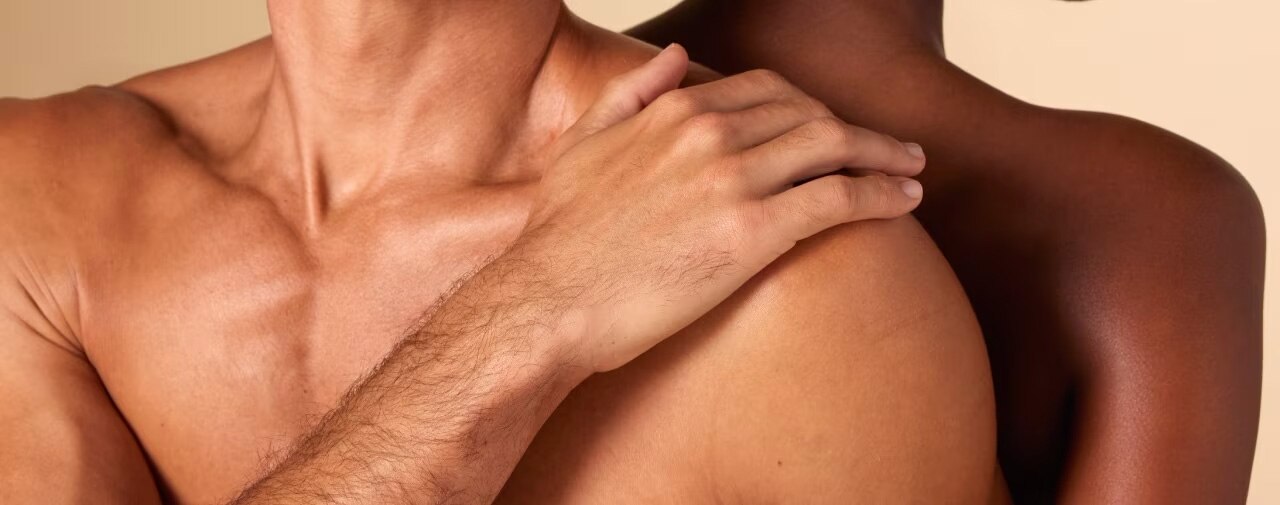 Intieme close-up van de schouders en borst van twee mensen. De hand van een persoon met een lichte huidskleur rust teder op de schouder van een persoon met een donkere huid.