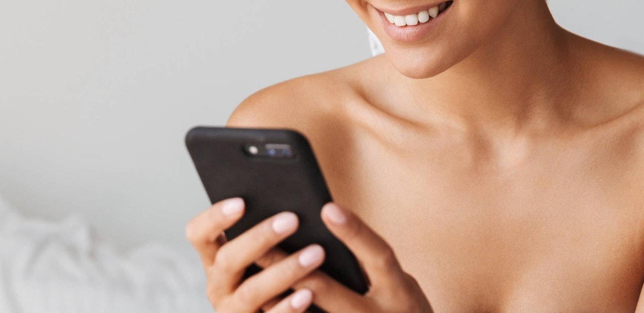 Vrouw glimlacht terwijl ze een smartphone vasthoudt en gebruikt.