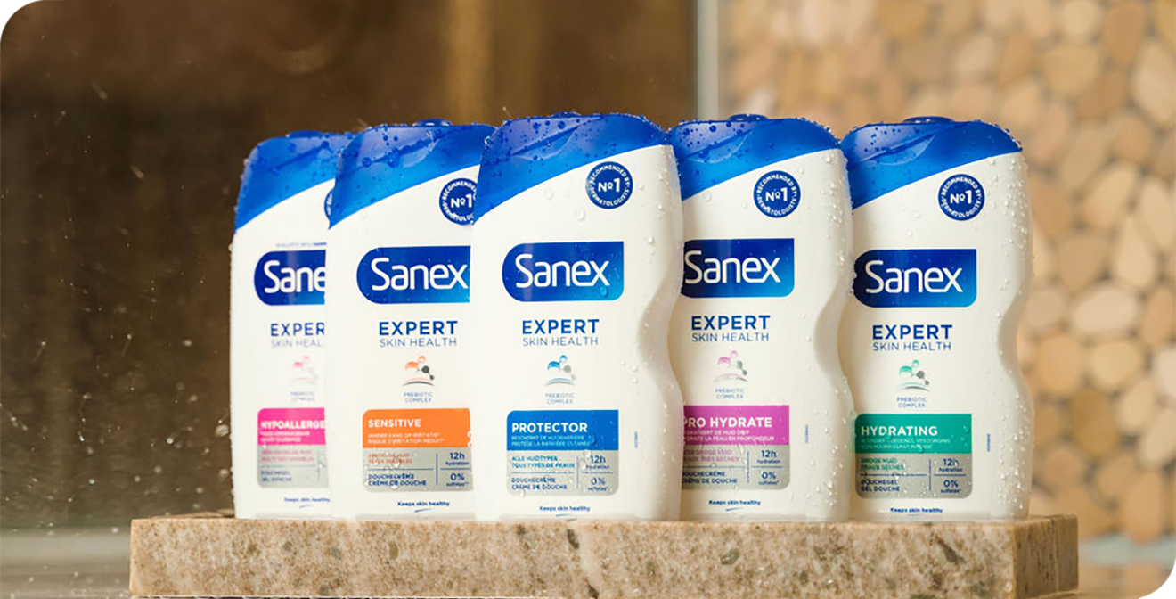Vier flessen Sanex Expert Skin Health douchegel staan op een rand in de badkamer." title="Vier flessen Sanex Expert Skin Health douchegel staan op een rand in de badkamer.