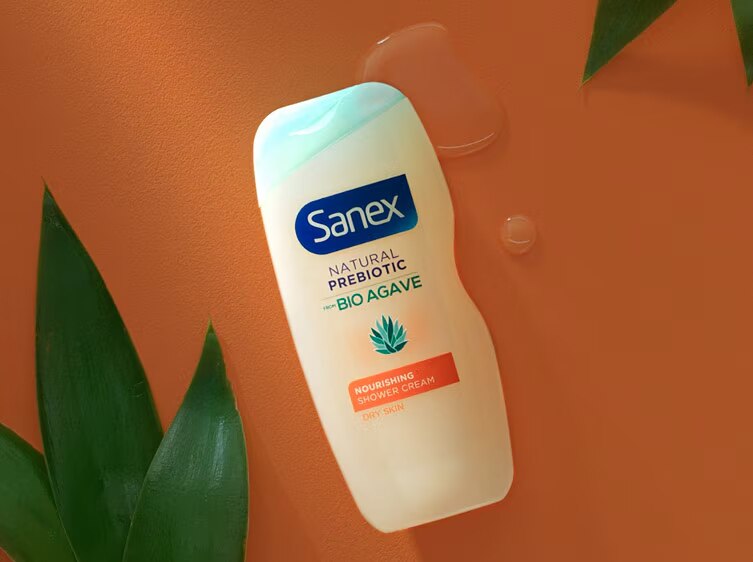 Sanex Natural Prebiotic Bio Agave Revitaliserende Douchegel met oranje label op een oranje achtergrond met groene bladeren.